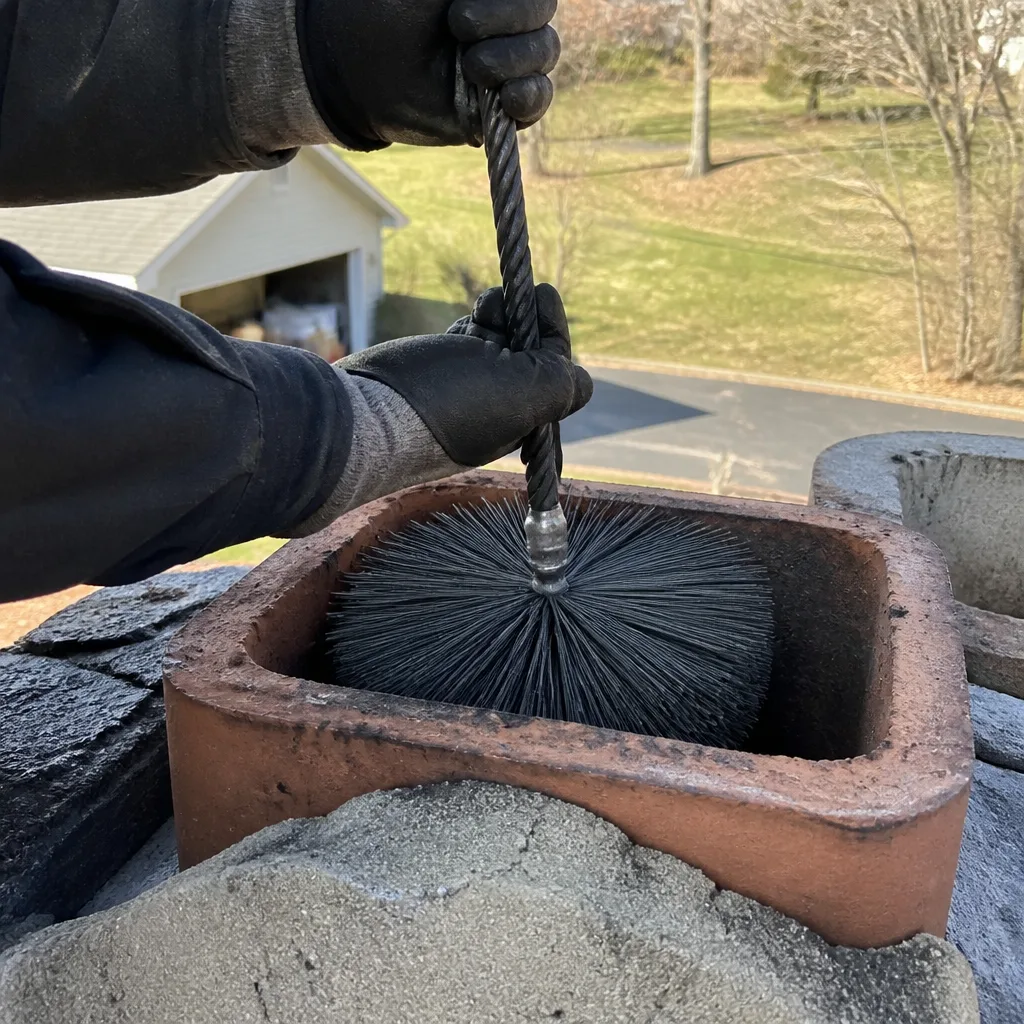 Professional chimney sweep cleaning a chimney flue with a wire brush
